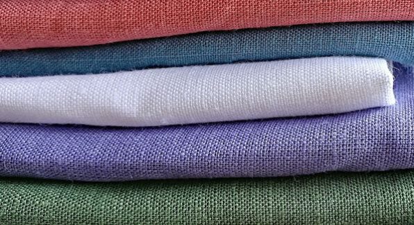 Stapeltje verschillende kleuren linnen stof in de kleuren groen, paars, wit. blauw en rood.